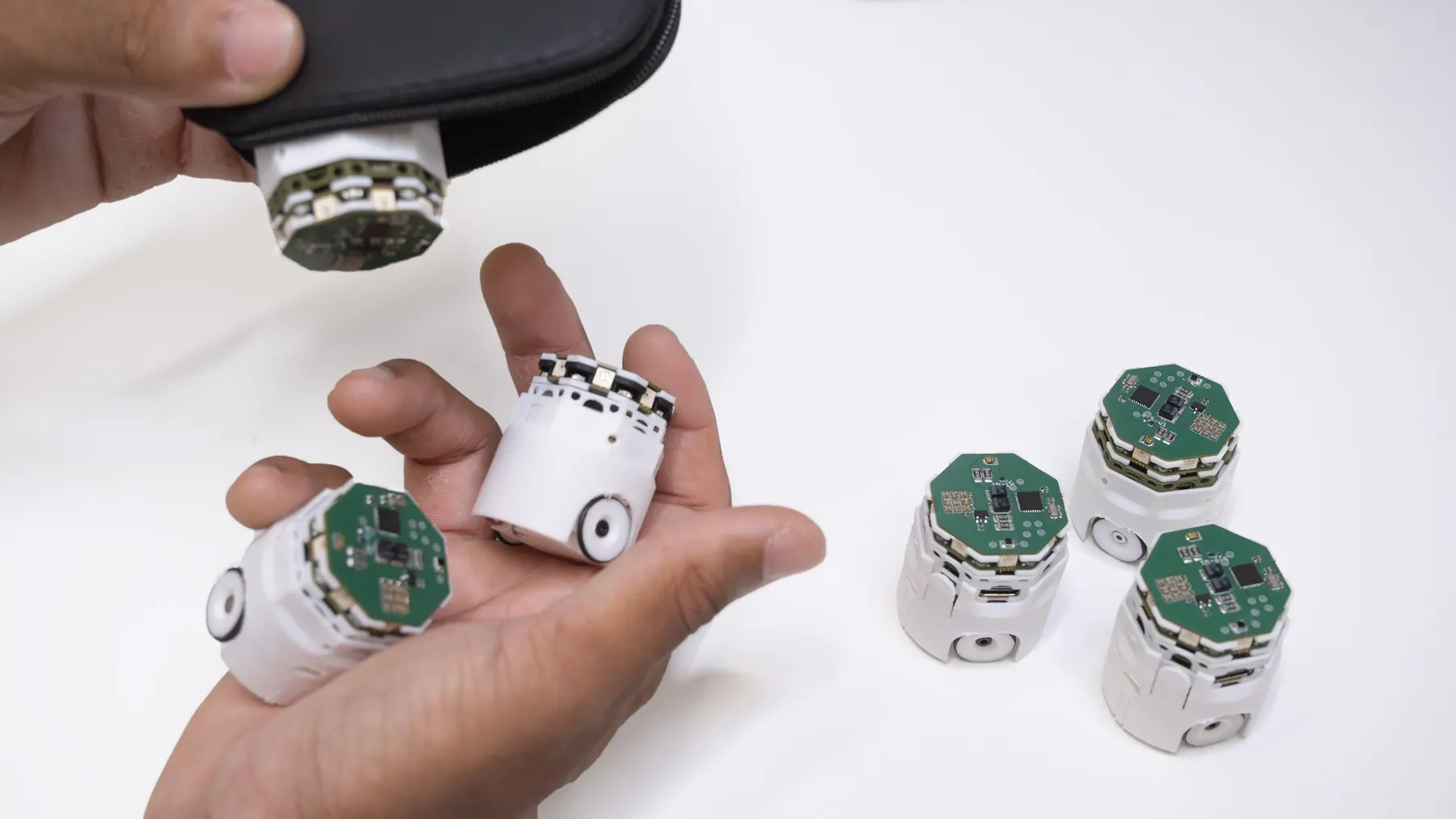 Robots being taken out of a small pouch and held in an open hand, with more robots on the table.