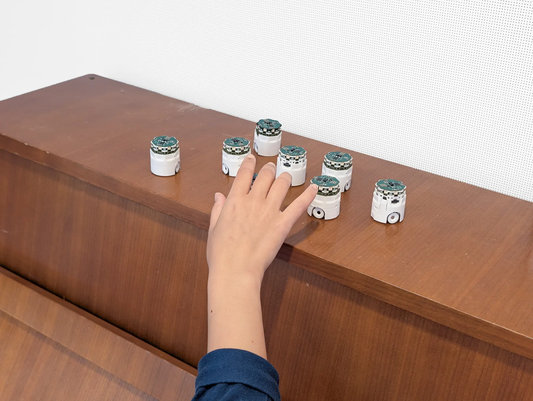 A child's hand reaching toward robots standing on top of an upright piano.